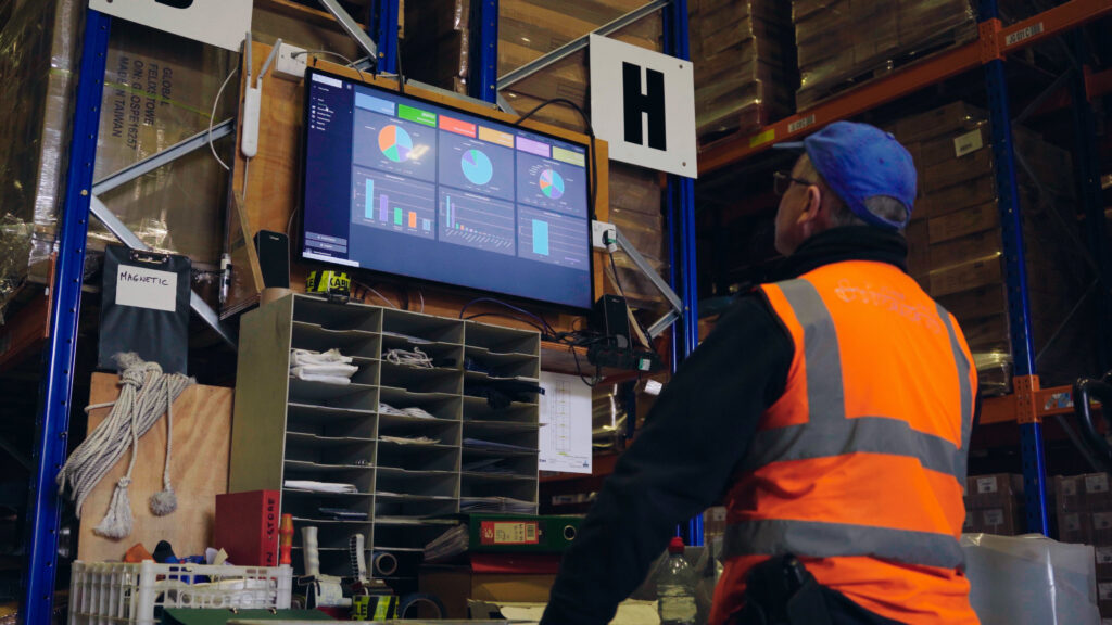 Clarus on screen | clarus wms Warehouse worker viewing a clarus wms dashboard with charts and kpis on a wall mounted screen